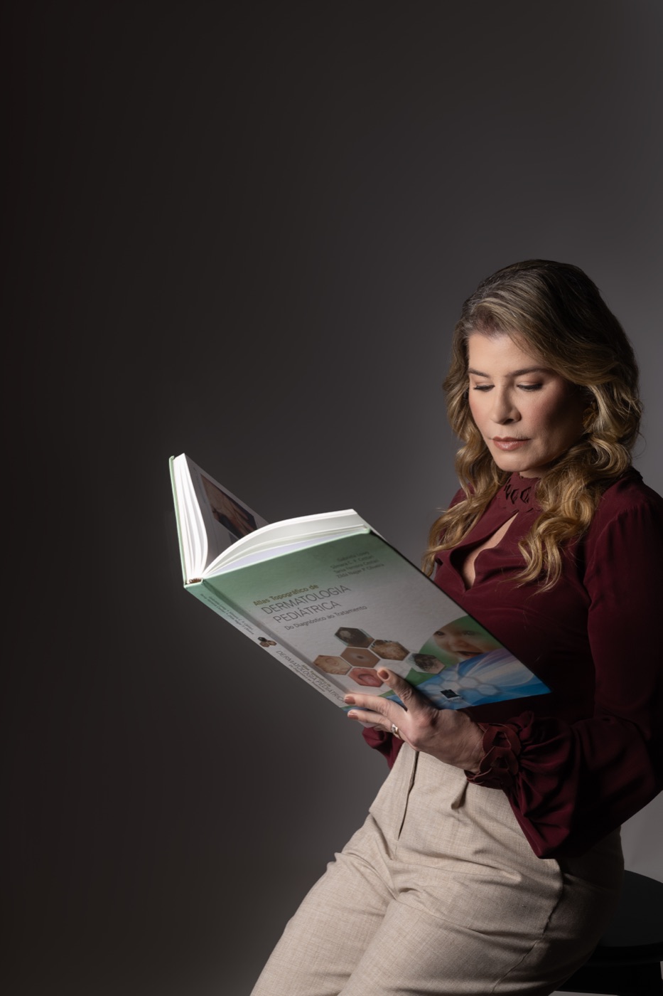 Dra. Bianca lendo o Atlas de Dermatologia Pediátrica sob luz dramática